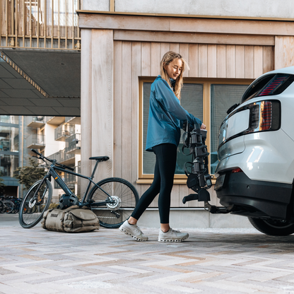 A woman is placing a Thule Outpace towbar bike carrier on the towbar on a white car.